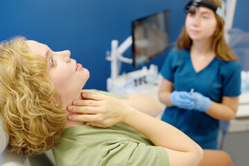 A young woman at an otolaryngologist's appointment talks about pain in the lymph nodes. A professional ENT doctor examines the patient