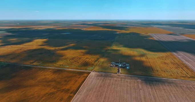 Shadows form clouds fall on the immense field. Drone approaches the little site with oil rig for drilling resources.
