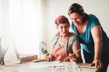 Gay senior couple painting with watercolor on art canvas at home. LGBT Lesbian family having fun together