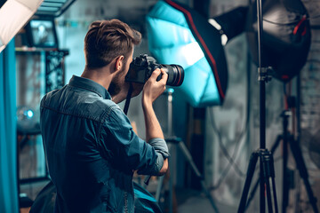 A photographer adjusting the settings on their camera in a studio, with various photography equipment in the background, showcasing the art of photography