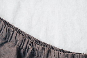 Natural dark brown linen pants on white linen fabric background. Top view. Sustainable, eco-friendly fashion