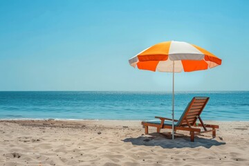 Fototapeta premium A peaceful ocean shore scene featuring a single beach chair paired with an orange and white striped umbrella set against the backdrop of a clear, blue ocean.