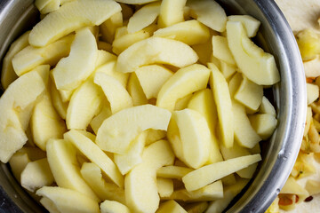 Close up view of gala apple slices in salt water in stainless bowl.  Preparation for a pie.  Scraps nearby.