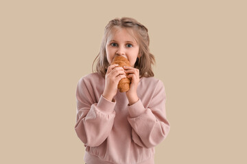 Cute little girl with croissant on beige background