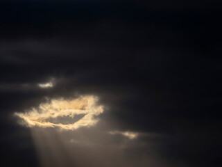 A dark sky with a sun rays shining through a cloud. Dramatic nature scene. Light creates an eye shape.