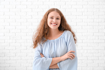 Portrait of happy redhead woman near white brick wall