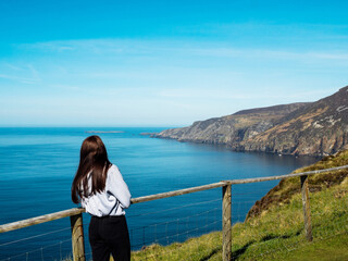 Young teenager girl exploring beautiful Sliabh Liag, county Donegal, Ireland. Travel and tourism. Warm sunny day. Stunning Irish nature landscape scene in the background.