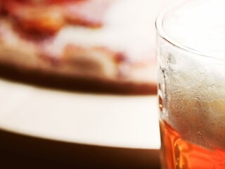 A glass of lager beer in focus. Italian cooked pizza out of focus in the background. Light and airy look.