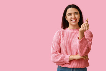 Beautiful young girl showing heart gesture on pink background. Valentine's Day celebration