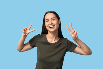 Beautiful young woman showing victory gesture on blue background