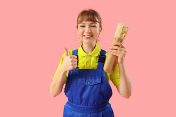 Female courier with doner kebab showing thumb-up on pink background