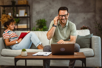 man listen music while work from home while woman read a book on sofa