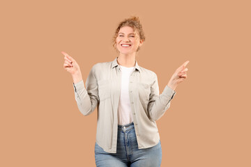 Beautiful young happy woman in stylish jeans pointing at something on beige background