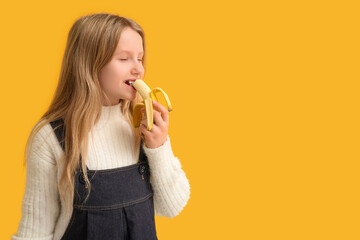 Cute little girl eating ripe banana on orange background