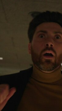 Footage of scared young bearded man in formal clothes running down hallway indoors. Shot of frightened guy in hotel at night. Shot with anamorphic lens. Cinematography technique