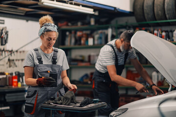 Female mechanic is putting working gloves on while repairman fixing car