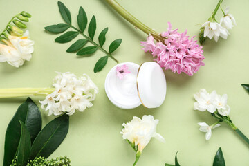 Composition with jar of cream and beautiful flowers on green background