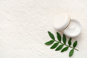 Jar of cream and plant leaf on light background