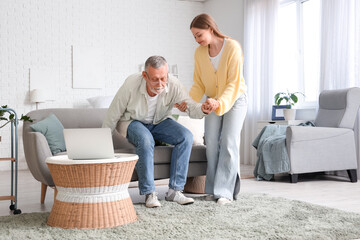 Female caregiver helping senior man to stand up from sofa in nursing home