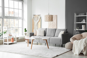 Stylish interior of living room with grey sofa, coffee table, armchair and blanket