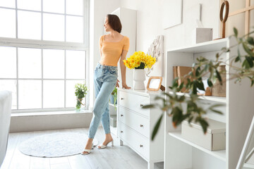Young woman with daffodils in vase on commode at home