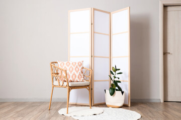 Interior of light room with folding screen, armchair and plant