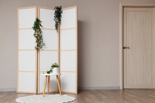 Folding screen with plants and table near light wall in room