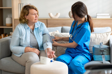 Nurse Providing Home Care to Elderly Woman, Checking Blood Pressure in Comfortable Living Room Setting