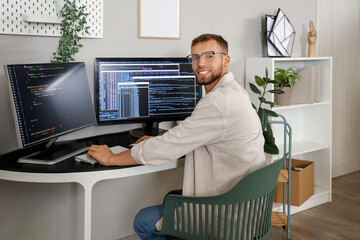 Young bearded programmer working with computer at table in office