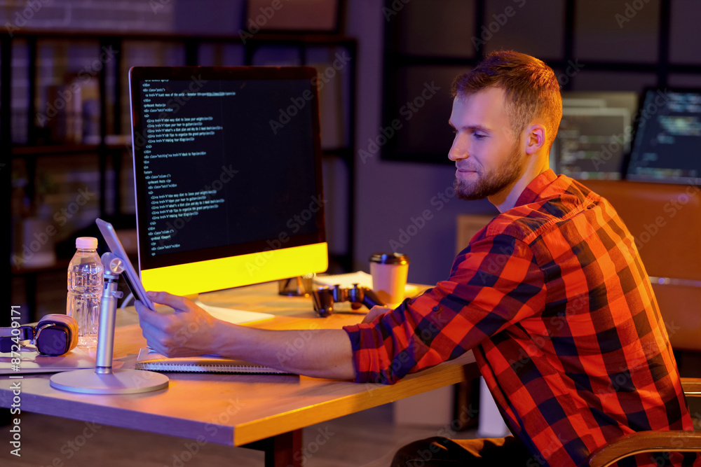 Poster Young bearded programmer working with tablet computer in office at night