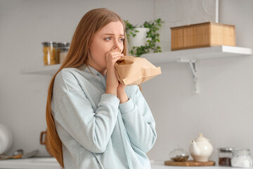 Young woman with paper bag having panic attack in kitchen