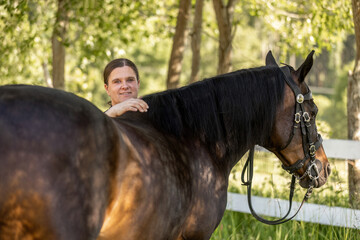 Portrait of a woman and her bay brown horse at a paddock in summer outdoors