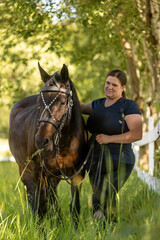 Portrait of a woman and her bay brown horse at a paddock in summer outdoors