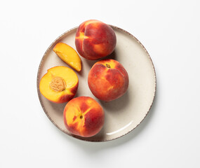 Fresh and vibrant peaches arranged on a beige plate against a clean white background. This appetizing image showcases ripe, juicy peaches perfect for healthy snacks and summer desserts. 