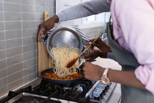 Cooking pasta together, couple pouring spaghetti into pan with tomato sauce