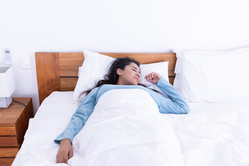 Sleeping peacefully, woman resting in bed with white sheets and wooden headboard