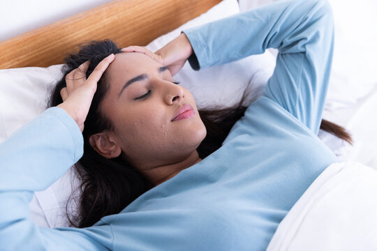 Relaxing in bed, woman with closed eyes massaging her temples