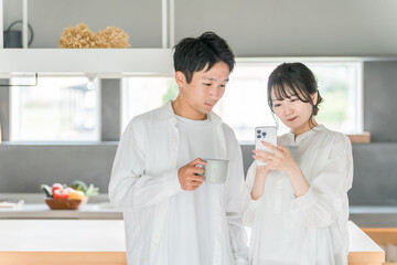 家のダイニングでコーヒーを飲みながらスマホを見る夫婦・カップル
