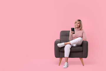 Happy woman with phone on armchair against pink background, space for text