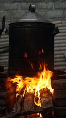 A fire burns in a wood burning stove with a black pot on top. Focus selected