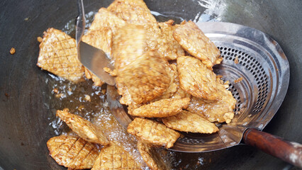 Fried tempeh is being fried in cooking oil on a wok. Focus selected