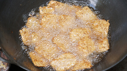 Fried tempeh is being fried in cooking oil on a wok. Focus selected