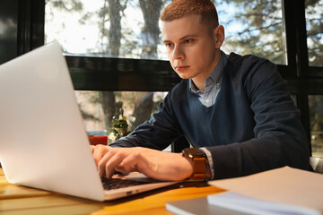 Young male student with laptop studying at table in cafe
