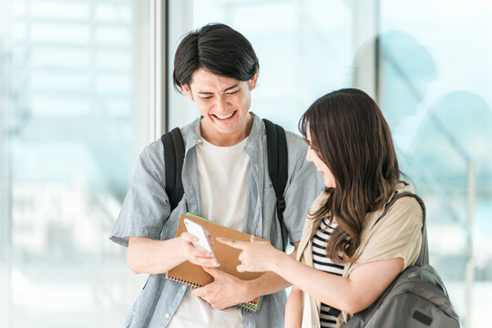 スマホを見ながら談笑する学生・大学生の男女（キャンパスライフ）
