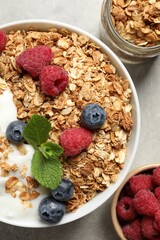 Tasty granola with berries and yogurt in bowl on grey textured table, flat lay