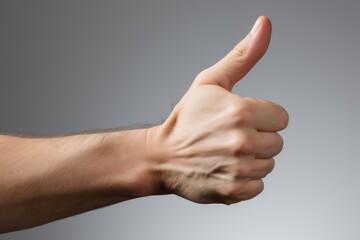 A stock image of a Caucasian male hand giving a thumbs up on a plain gray background. The hand is well-lit with smooth skin, thumb extended, other fingers curled in