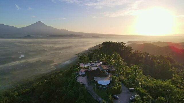 Beautiful view of Enam Langit Plataran restaurant on the top of hill with mountain background in sunrise time. 4K aerial drone view.
