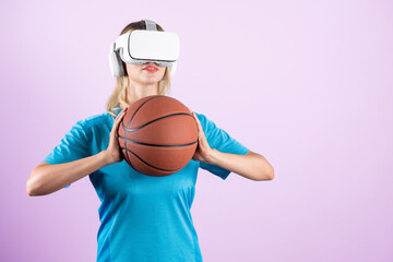 Girl wearing visual reality glasses and casual cloth and holding basketball. Caucasian woman playing basketball while standing at pink background at sport arena hologram. Innovation. Contraption.