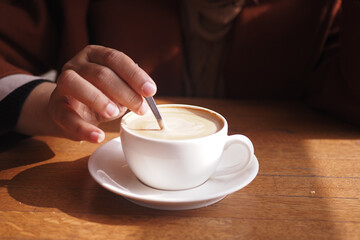 person hand stirring coffee with spoon.