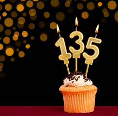 Birthday candle with cupcake - Number 135 on black background with out of focus lights